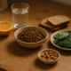 Bols en céramique avec lentilles, épinards, amandes, une orange coupée et deux tranches de pain complet.