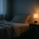 Chambre nocturne avec lit défait, lampe de chevet allumée, lunettes et verre d'eau
