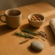 Tasse fumante, bol d'amandes et graines, brins de romarin et lavande, galet et linge sur bois