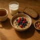 Bol de porridge aux fruits rouges entouré d'une tranche de pain, d'un verre de lait et d'un thé
