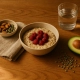 Bol de flocons d'avoine garni de framboises, avocat, lentilles vertes et amandes sur table en bois.
