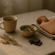 Tisane fumante, bol d'amandes et légumineuses, carrés de chocolat noir et bouillotte posés sur une table en lin